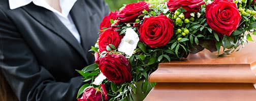 Blumenkranz mit roten Rosen werden auf einen Sarg gelegt