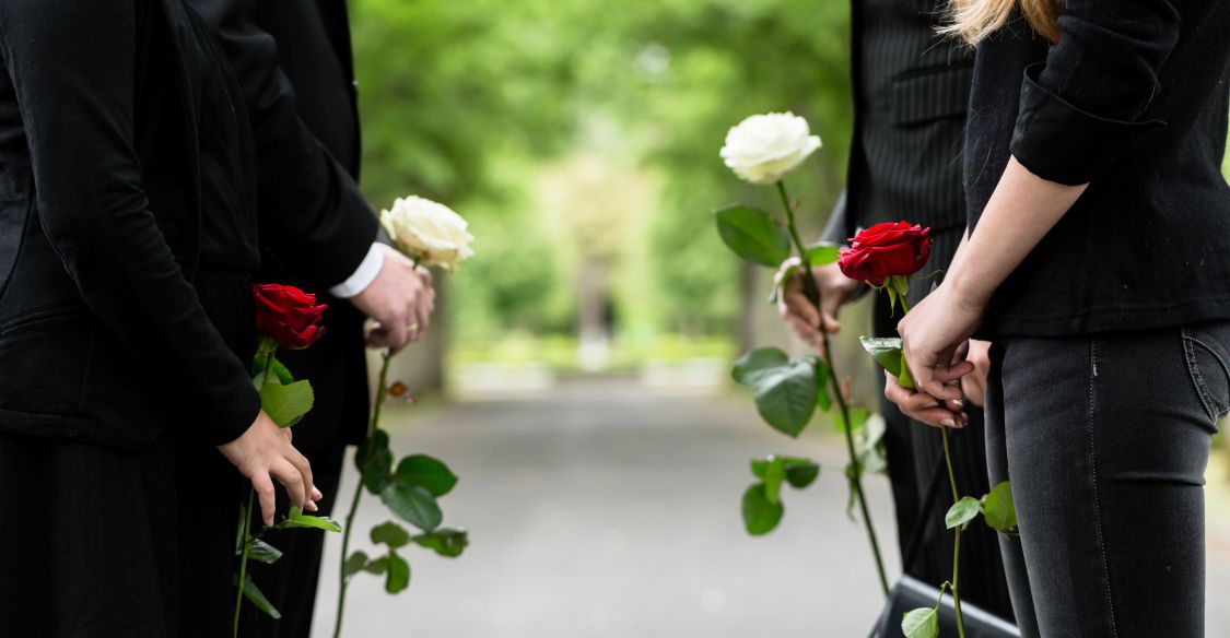 Vier Personen mit Rose bei einer Trauerfeier